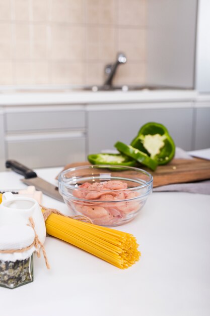 Сырые спагетти; курица в миске и нарезанный перец на столе