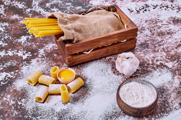 Raw spaghetti and macaroni with flour on wooden table. 