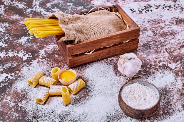 Raw spaghetti and macaroni with flour on wooden table. 