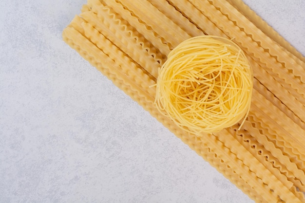 Raw spaghetti nest and pasta on marble table.