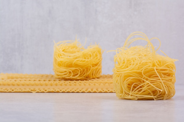 Raw spaghetti nest and pasta on stone surface