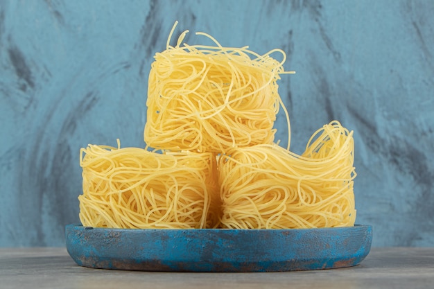 Raw spaghetti nests on blue plate.