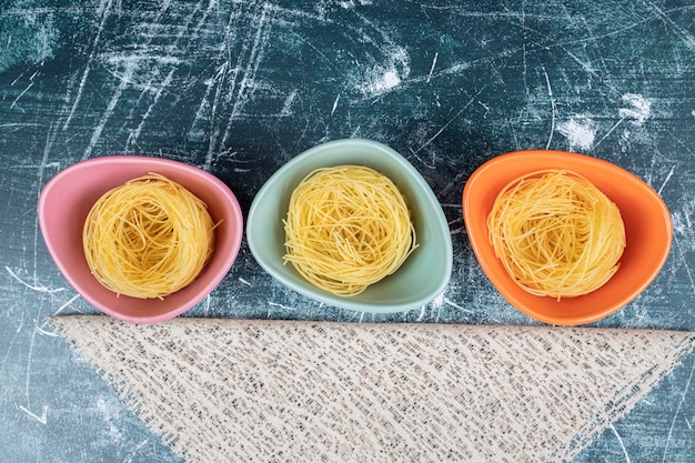 Foto gratuita nidi di spaghetti crudi in ciotole colorate e tela. foto di alta qualità