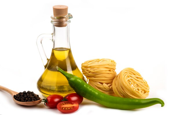 Сырые гнезда спагетти, свежие овощи и бутылка масла на белом.