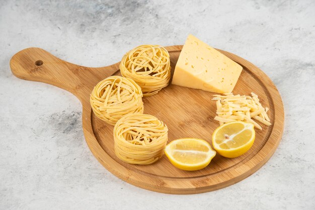 Raw spaghetti nests, lemonnd cheese wooden board.