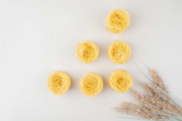 Raw spaghetti nests on white surface with wheat