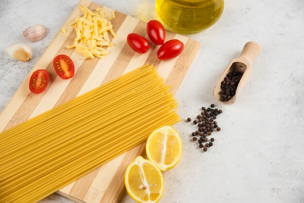 Raw spaghetti, oil and fresh vegetables on wooden board.