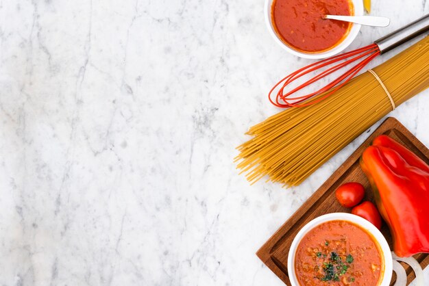 Raw spaghetti pasta and sauce with fresh tomatoes on marble textured background