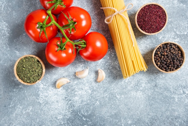 Бесплатное фото Сырые спагетти, специи и помидоры на мраморном фоне.