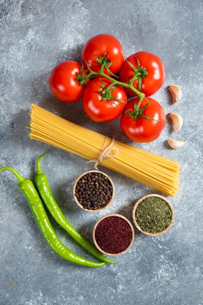 Raw spaghetti, spices and tomatoes on marble background.