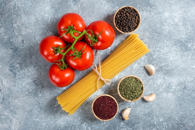 Spaghetti crudi, spezie e pomodori su fondo di marmo.