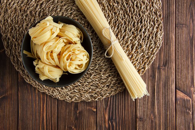 Raw spaghetti with fettuccine pasta flat lay on wooden and wicker placemat background