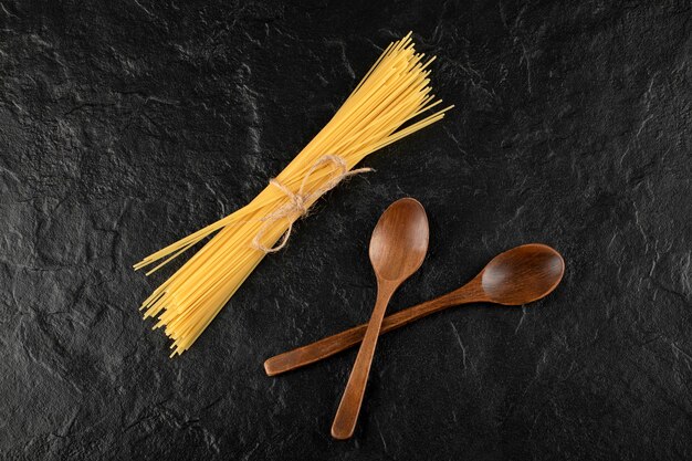 Raw spaghetti and wooden spoons on black surface