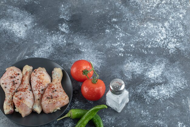 Raw spicy chicken drumstick with tomato, pepper and salt on grey background.