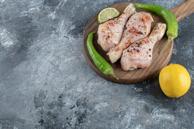 Raw spicy chicken drumsticks with green pepper and lemon.