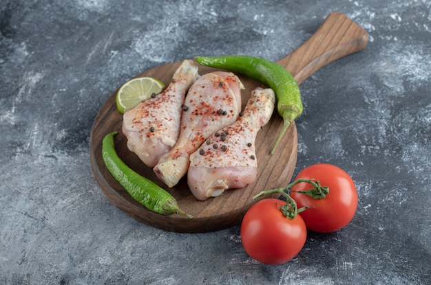 Raw spicy chicken drumsticks with green pepper and tomatoes over grey background.