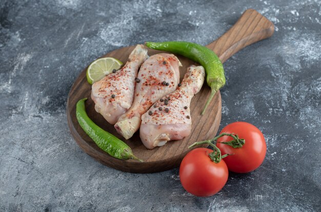 raw spicy chicken drumsticks with green pepper and tomatoes over grey background.