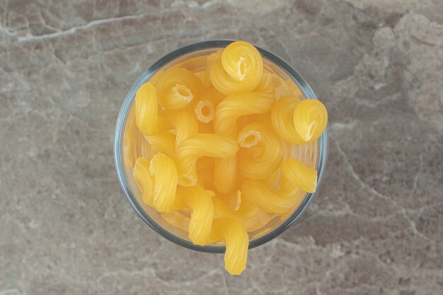 Raw spiral pasta in glass on marble surface.