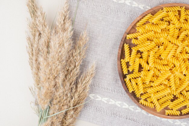 Raw spiral pasta on wooden plate with wheat