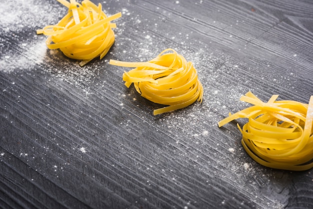 Raw tagliatelle dusted with white flour on wooden background