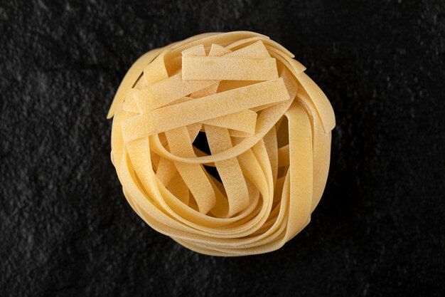 Raw tagliatelle nests on black surface