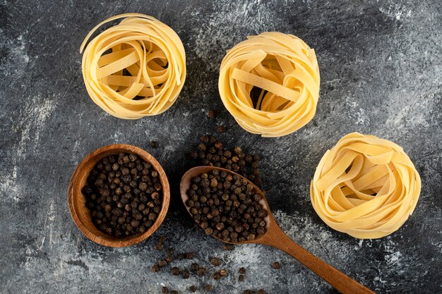 Raw tagliatelle nests and pepper grains on marble surface