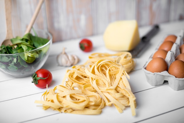 Raw tagliatelle pasta and ingredient over wooden table