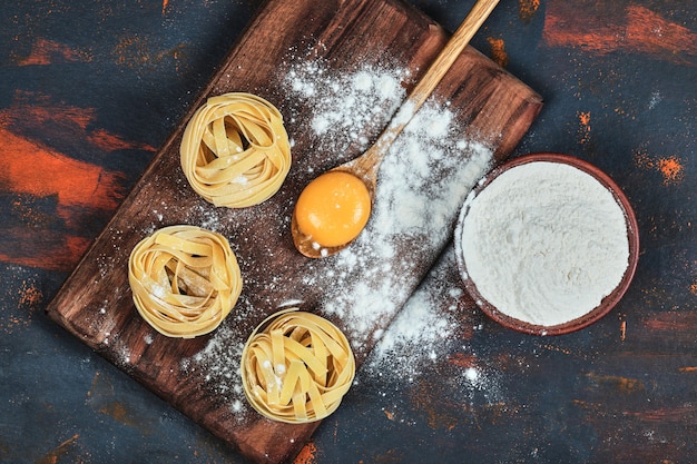 Free photo raw tagliatelle pasta on wooden board with bowl of powder.