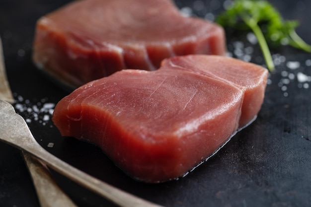 Raw tuna slices with salt on dark background.