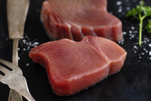 Raw tuna slices with salt on dark background
