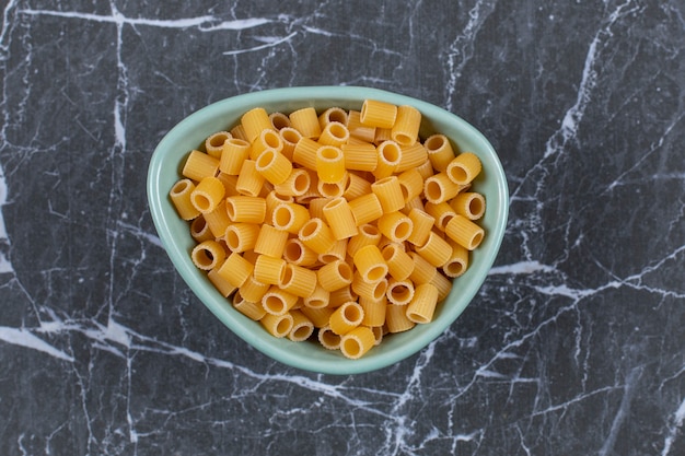 Raw uncooked penne pasta in blue bowl.