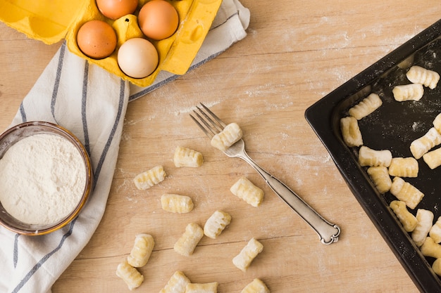 Raw uncooked potato gnocchi with flour and eggs on wooden desk