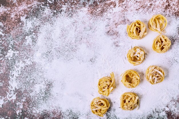 Raw uncooked tagliatelle pasta on wooden kitchen table. 