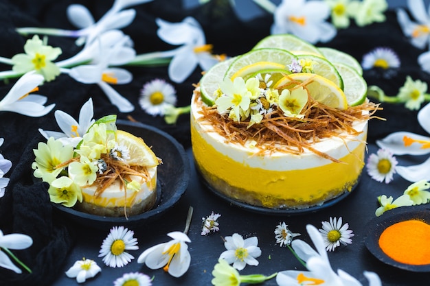 Raw vegan cake with lemon and lime on a black surface covered with tiny daisy flowers