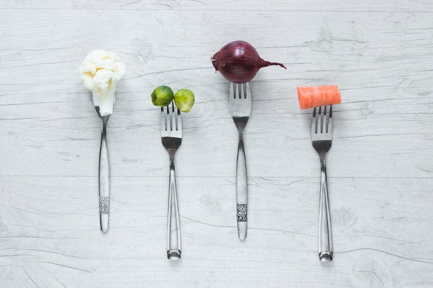 Free photo raw vegetables on fork arranged in a row on wooden table