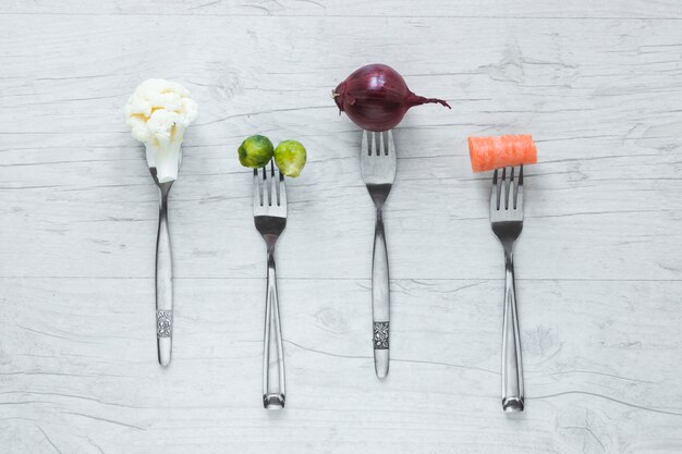 Raw vegetables on fork arranged in a row on wooden table