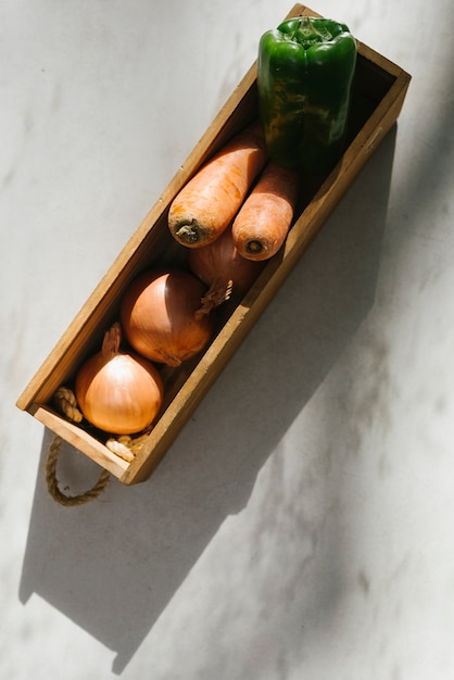 Raw vegetables in wooden tray on marble