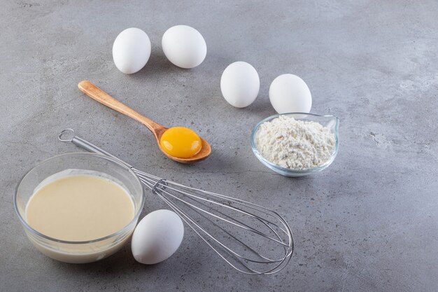 밀가루와 우유와 함께 원시 흰색 닭고기 달걀을 돌 테이블에 배치합니다.