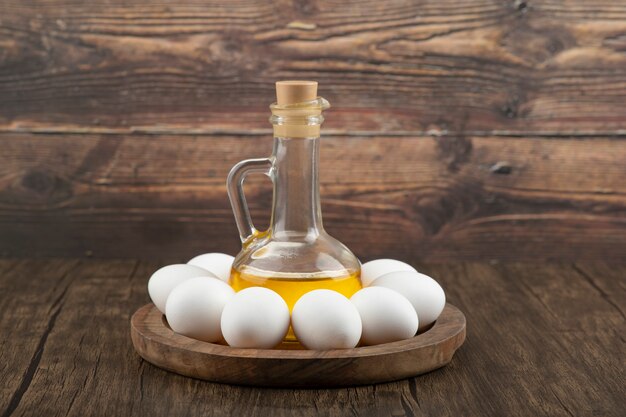 Raw white eggs and bottle of olive oil on wooden board.