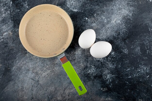 Raw white eggs next to empty pan. 