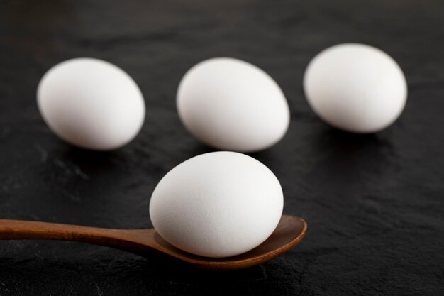 Raw white eggs and wooden spoon on black surface. 