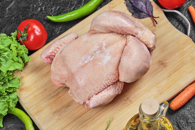 Raw whole chicken on wooden board with lettuce, peppers, oil and tomatoes 