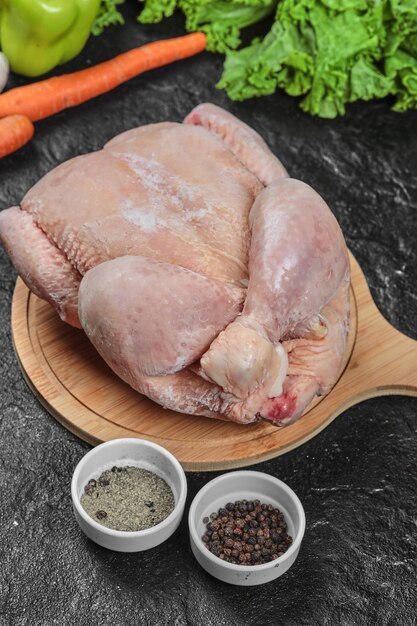 Raw whole chicken on wooden board with vegetables and spices