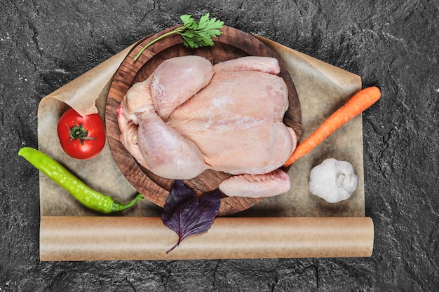 Raw whole chicken on wooden plate with fresh vegetables