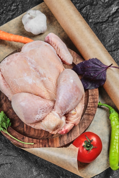 Raw whole chicken on wooden plate with fresh vegetables