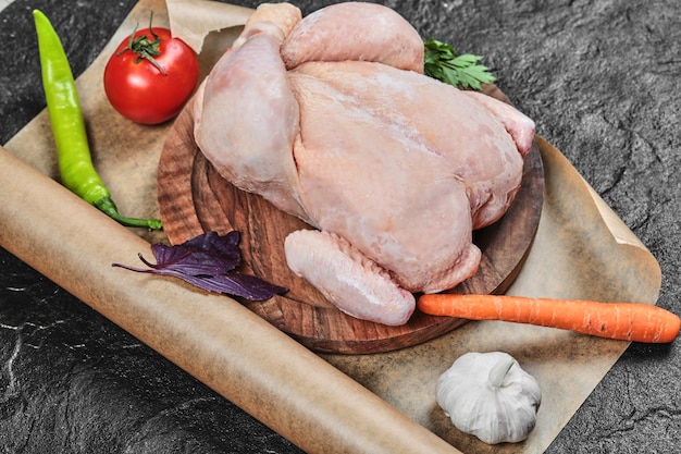 Free photo raw whole chicken on wooden plate with fresh vegetables