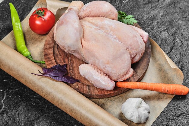 Сырая целая курица на деревянной тарелке со свежими овощами