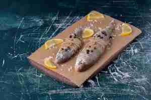 Бесплатное фото Сырые целые рыбы с ломтиками лимона, перцем и солью на деревянной доске.