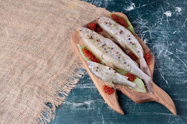 Raw whole fishes with red caviar on wooden board. 