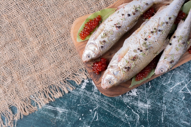 Raw whole fishes with red caviar on wooden board. 